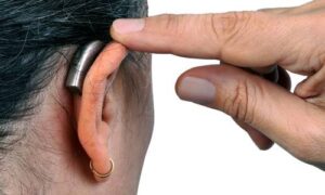 a finger pointing to a hearing aid in a woman's ear